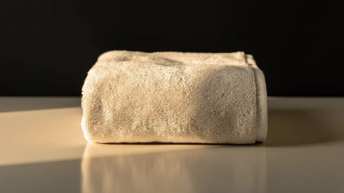Folded cream towel lit by soft warm daylight against a dark background